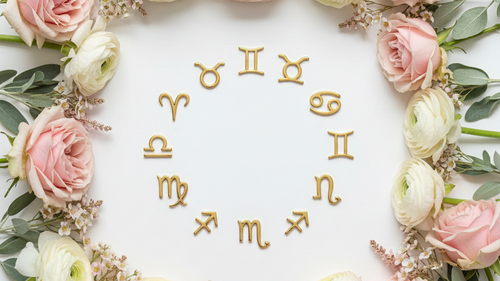 Gold zodiac symbols arranged in a circle on a white background, framed by pink and white roses with green foliage.