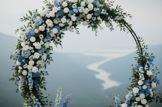 Lush blue wedding floral arch overflowing with farm-fresh blue hydrangeas, delphinium, white garden roses, lisianthus, eryngium, and light blue limonium with a soft mountain backdrop