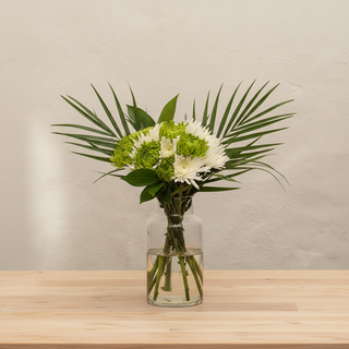 Hand-tied spider mum bouquet with green and white anastasia spider mums cocculus and robellini palm fronds in a clear glass vase on a wooden table from Bloomingmore