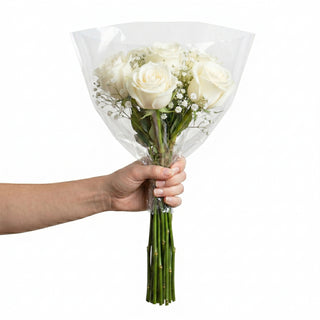 Hand holding a bouquet of white roses wrapped in clear plastic against a white background