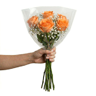 Hand holding a bouquet of orange roses wrapped in clear plastic on a white background