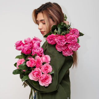 A woman holding two large bouquets of vibrant Hot pink Mayra Garden Roses with green leaves 