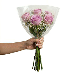 Hand holding a bouquet of lavender roses wrapped in clear plastic on a white background